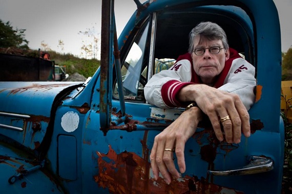 Stephen King sentado no banco do motorista de em uma caminhonete azul e olhando pela janela