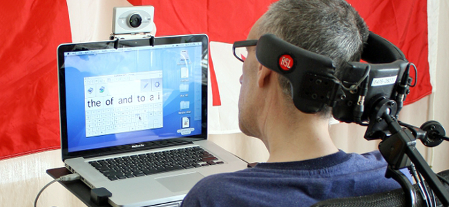 Homem com deficiência física está de costas, com a cabeça apoiada, utilizando o computador