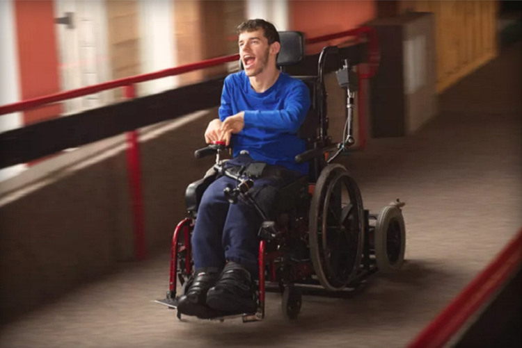 Homem jovem com deficiência em cadeira de rodas automatizada em corredor iluminado