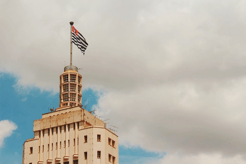 Foto do topo do edifício Altino Arantes, com a bandeira do Estado de São Paulo hasteada e tremulando