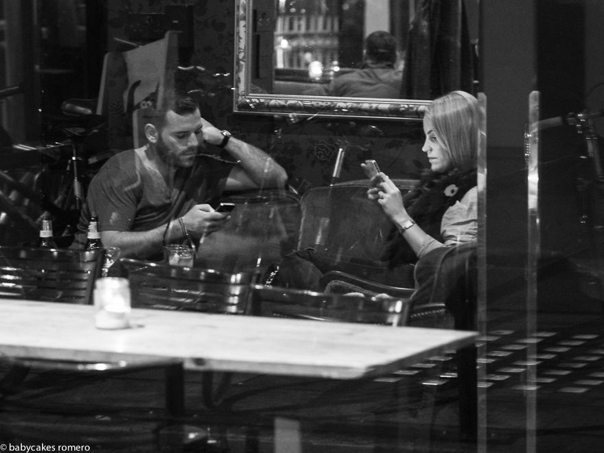 Casal em mesa de bar, cada um olhando para seu próprio aparelho smartphone